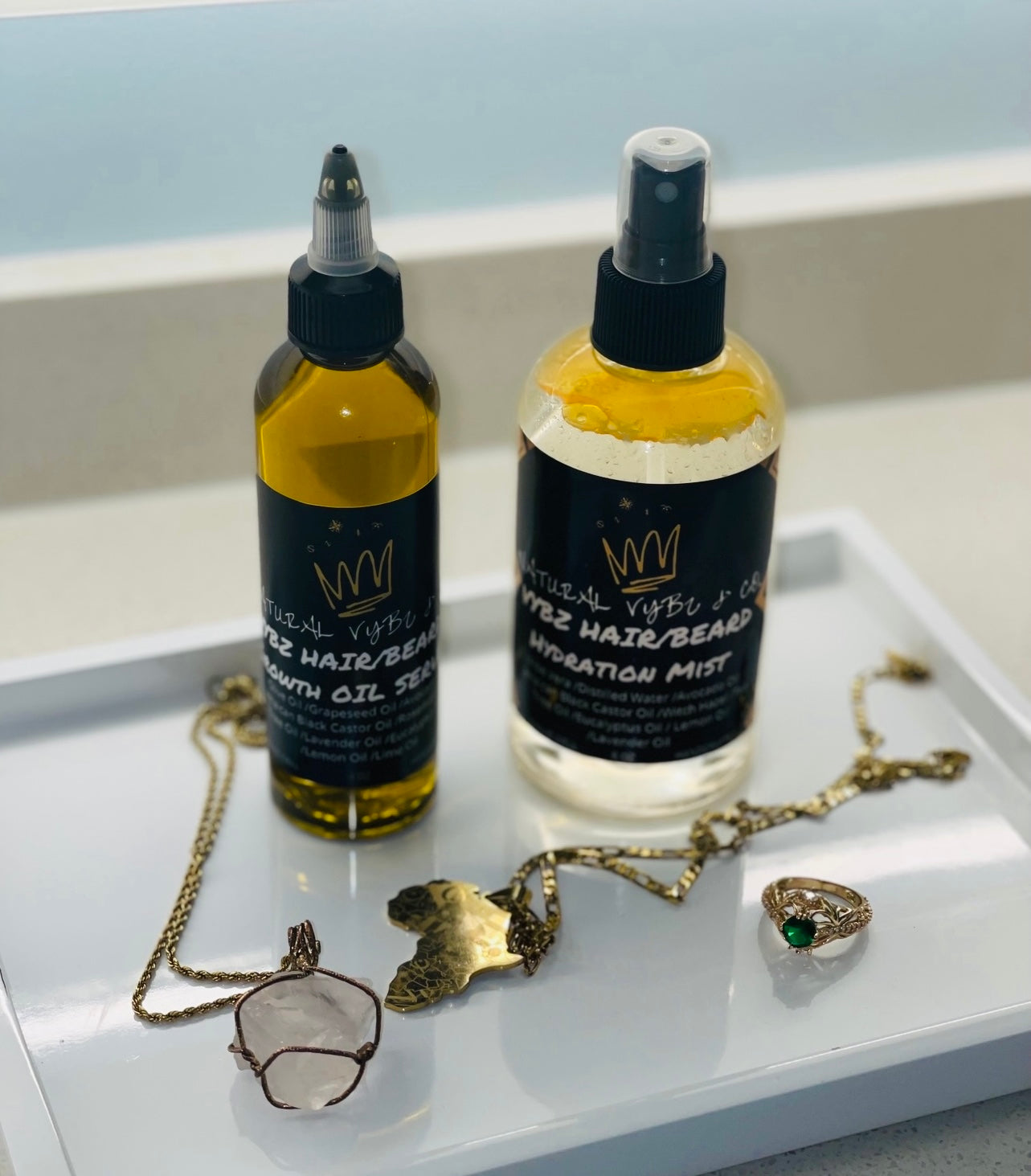 beard care products natural vybz beard oil and natural vybz beard mist in tray on bathroom counter with gold necklaces and a gold ring surrounding natural vybz products